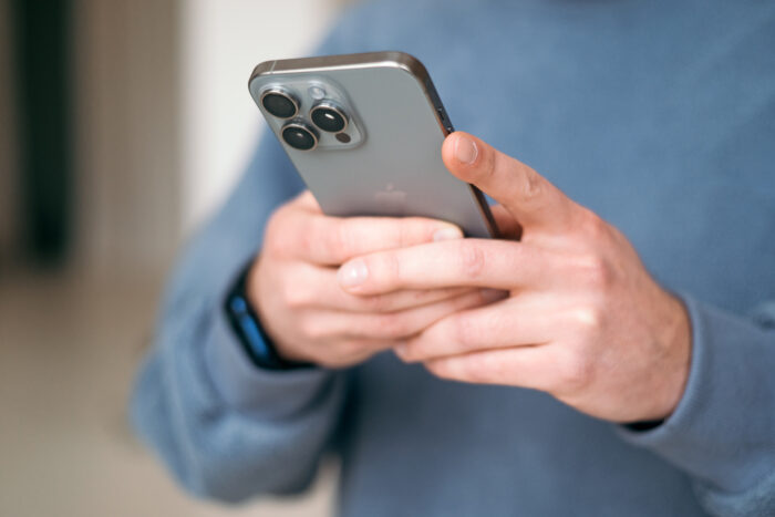  Man using a new mobile phone, iphone 15 smartphone close-up, holding cellphone in hands. texting message, scrolling