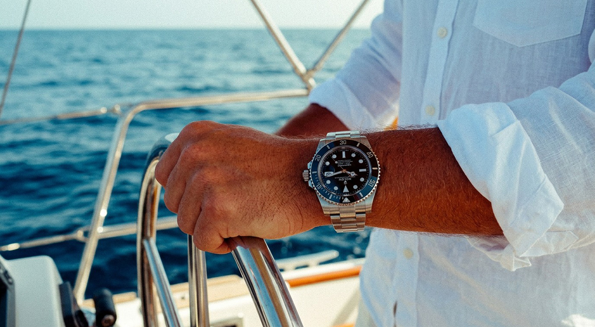 AI-generated image of Rolex prominently displayed on the wrist of a person navigating a sailboat at sea. The white linen shirt, polished metal details, and deep blue ocean backdrop evoke a sense of leisure, craftsmanship, and refined coastal living.