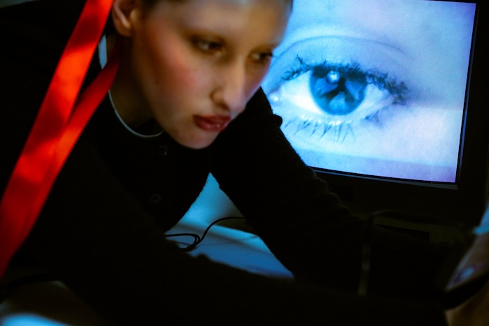 Woman with a camera whose feed is appearing on a CRT behind her