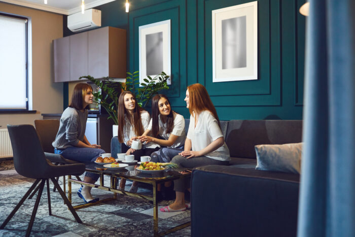 Charming casual women sitting on sofa in modern interior having tea and chatting