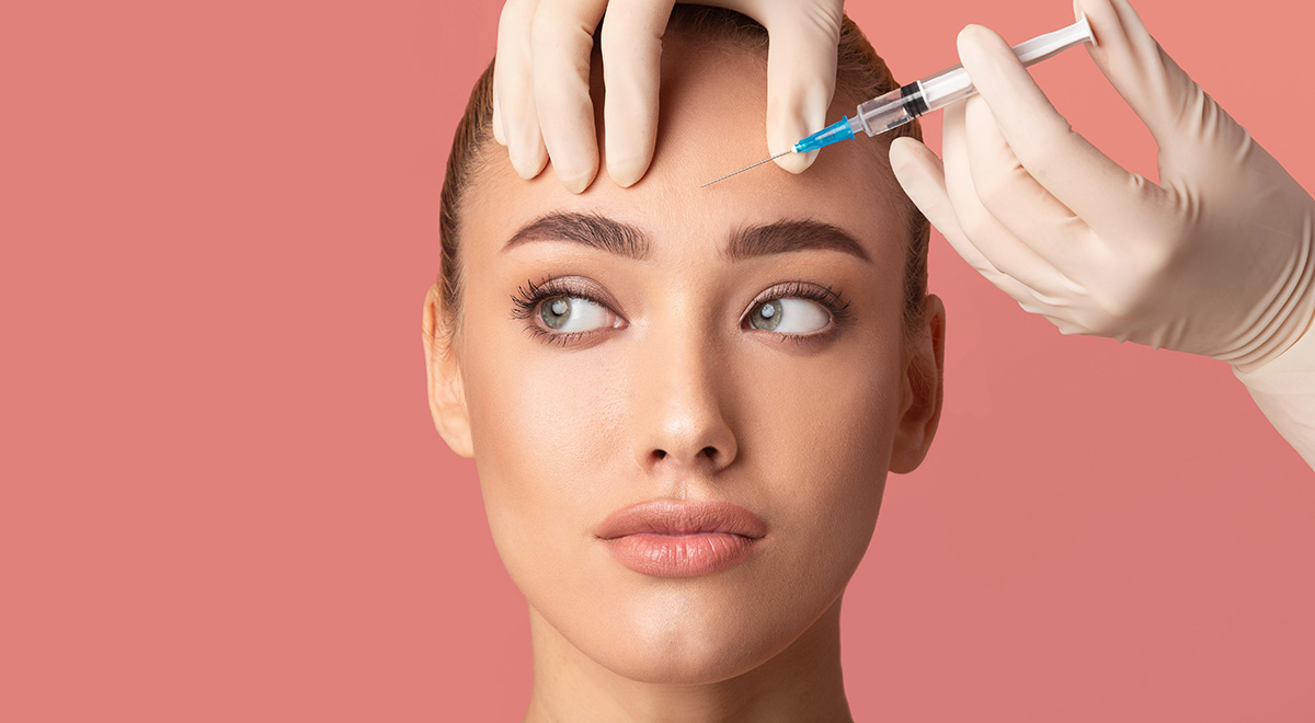 Woman receiving a cosmetic injection in her forehead from a practitioner wearing medical gloves.