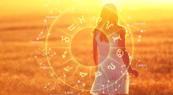 A glowing zodiac wheel and constellation graphics overlay the silhouette of a woman standing in a sunlit field at golden hour. The twelve astrological signs surround the scene, creating a dreamy, celestial illustration symbolizing romance, astrology, and personal insight.