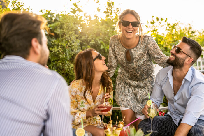young group of 30s people having fun at a cocktail party outdoor, beautiful women smiling and laughing with friends, handsome men talking with elegant female millenials