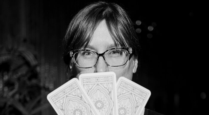 Cheese fortune teller Jennifer Billock holds three fortune-telling cards in front of her face in a black-and-white portrait.